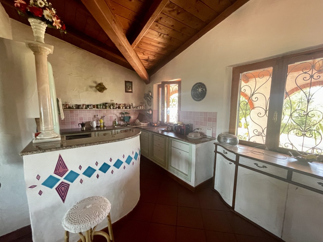 Cucina di campagna affascinante con bancone curvo e struttura in legno rustico - zona cottura luminosa con finestre decorative e ambiente con piani di lavoro in granito eleganti Cucina di campagna affascinante con bancone curvo e struttura in legno rustico - zona cottura luminosa con finestre decorative e ambiente con piani di lavoro in granito eleganti